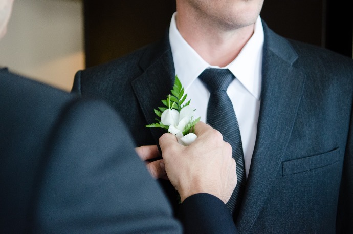 man attaching flower on another man's lapel in a well-lit room